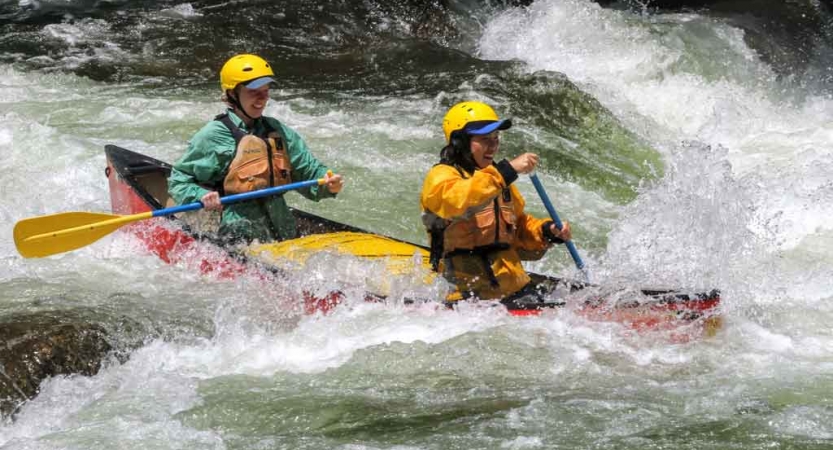two students in a canoe navigate whitewater in north carolina on an outward bound trip